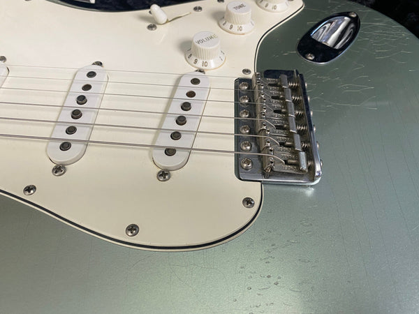 Close-up of Fender Stratocaster electric guitar bridge, white pickguard, volume and tone knobs, and single-coil pickups on seafoam green body