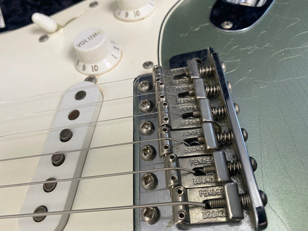 Close-up view of Fender electric guitar bridge and volume knob with white pickguard and strings for sale at Coffee House Guitars