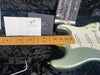 Close-up of Fender Stratocaster electric guitar neck and body in metallic seafoam green finish with white pickguard, included owner's manual, Fender 5-position pickup selector switch instructions, and tremolo arm resting on black plush guitar case interior.