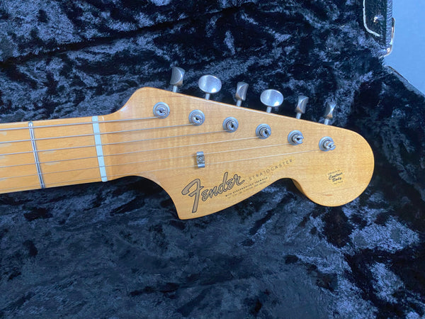 Close-up of Fender Stratocaster guitar headstock with tuning pegs on black plush guitar case interior