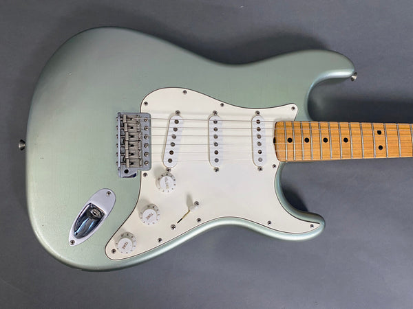 Close-up of vintage seafoam green electric guitar body with white pickguard, three single-coil pickups, volume and tone control knobs, chrome bridge, and maple fingerboard.