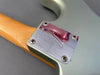 Close-up of Fender guitar neck plate with serial number R258656 on metallic green body and maple neck, showing four screws and minor wear chips.