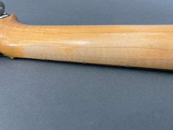 Close-up of guitar neck side showing small metal fret markers on a natural wood finish neck against a gray background