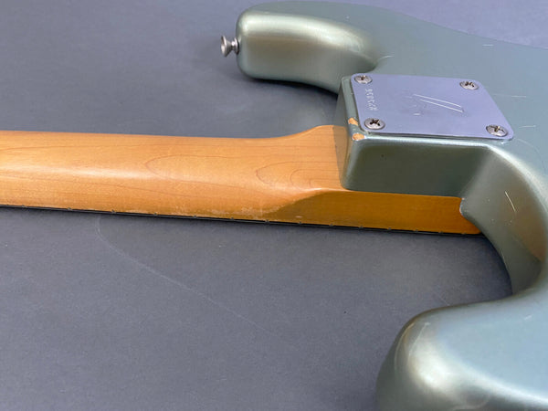 Close-up of maple neck joint and seafoam green guitar body with metal neck plate on electric guitar showing wood grain and body finish
