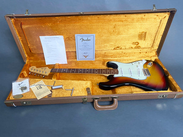 Fender Stratocaster electric guitar in sunburst finish inside vintage brown hard case with yellow plush interior, certificate of authenticity, warranty papers, and tremolo arm accessories