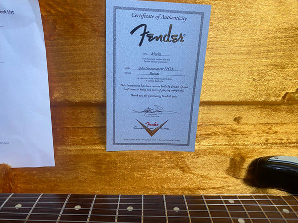 Fender Certificate of Authenticity for 1960 Stratocaster NOS with serial number R15043 displayed on orange plush guitar case lining with partial view of black Fender Stratocaster fingerboard and body.