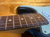 Close-up of electric guitar fretboard with dot inlays and steel strings on light blue and black body