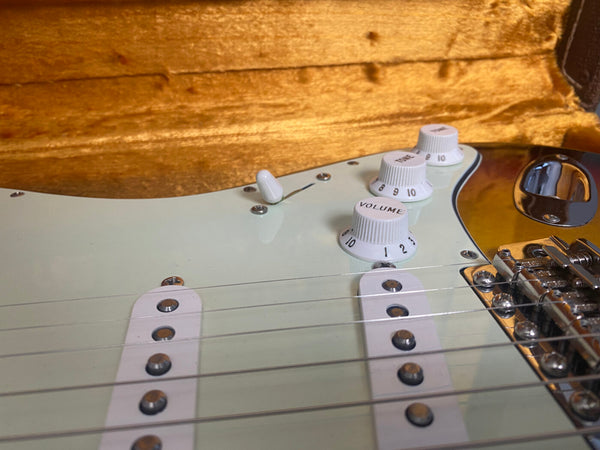 Close-up of white electric guitar control knobs labeled volume and tone with pickups and strings in an open guitar case with plush orange lining
