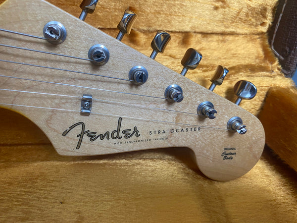 Close-up of Fender Stratocaster maple guitar headstock with tuning pegs and strings in a yellow plush guitar case