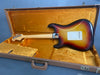 Sunburst electric guitar with maple neck resting in vintage orange plush-lined brown hardshell case shown from the back.
