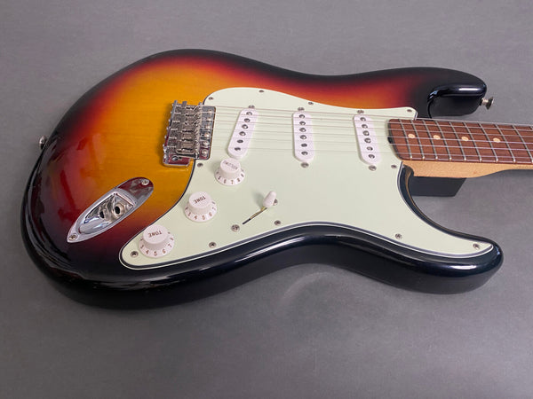 Electric guitar with sunburst finish, three single-coil pickups, white pickguard, volume and tone control knobs, and rosewood fretboard on a gray background