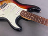 Close-up of sunburst electric guitar body and rosewood fretboard with white pickguard and single-coil pickups on gray background