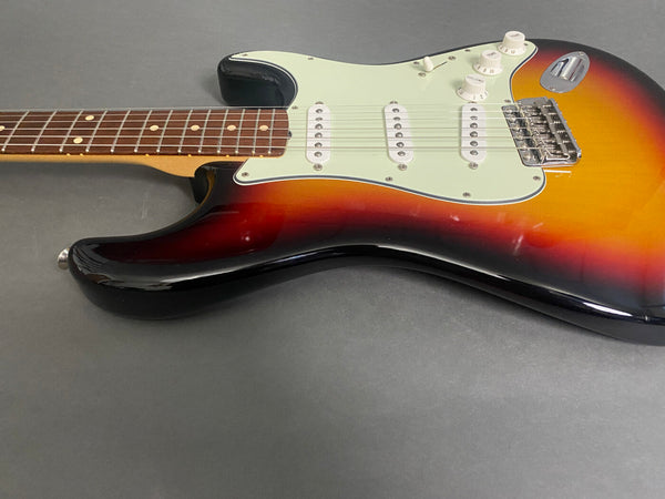 Sunburst electric guitar body with white pickguard, three single-coil pickups, and rosewood fretboard on gray background