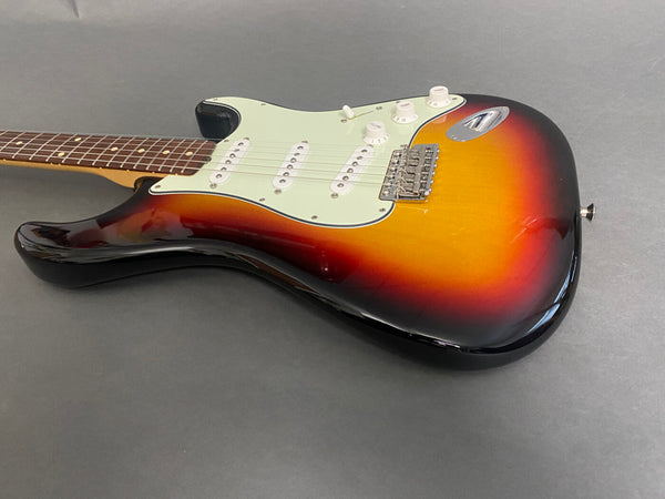 Sunburst electric guitar with white pickguard and three single-coil pickups on gray background