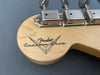 Close-up of Fender Custom Shop logo and tuning pegs on light maple guitar headstock with gray background