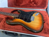 Vintage electric guitar with sunburst finish, rosewood fretboard, and black pickguard resting in red plush lined hard case
