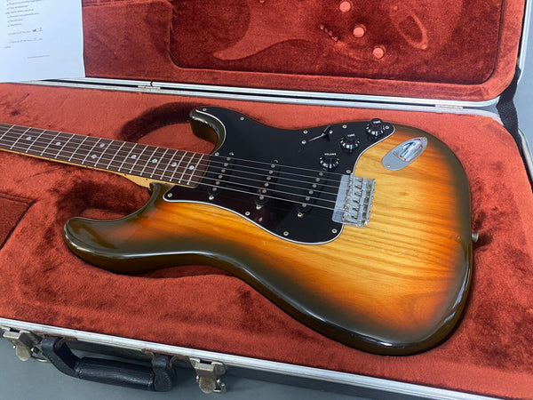 Vintage electric guitar with sunburst finish, rosewood fretboard, and black pickguard resting in red plush lined hard case