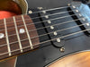 Close-up of acoustic guitar fretboard and black electric guitar pickups with strings over a wooden guitar body edge