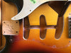 Close-up of vintage sunburst electric guitar body with cavity routed for pickups, showing signature and "MK" marking inside the guitar body.