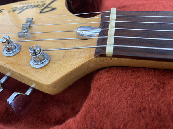 Close-up of Fender Stratocaster guitar headstock showing tuning pegs, strings, and nut on a red fabric background