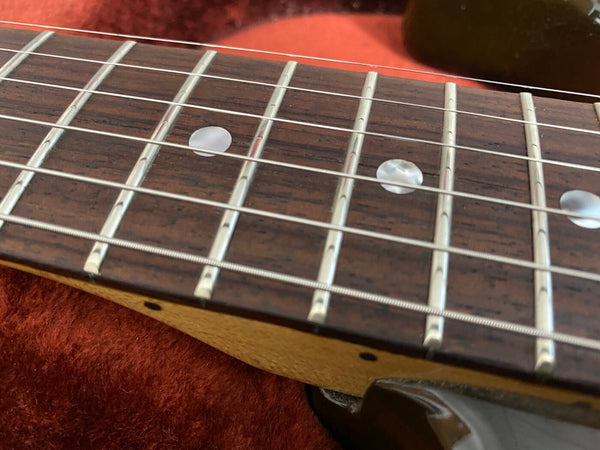 Close-up of guitar fretboard showing polished frets, pearl dot inlays, and metal strings on a rosewood neck.