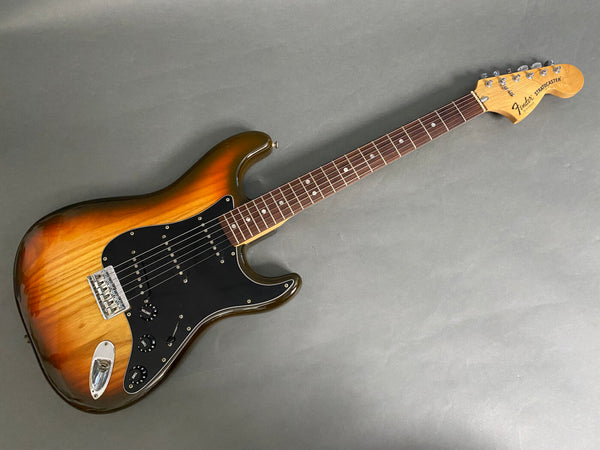 Fender Stratocaster electric guitar with sunburst finish, black pickguard, and rosewood fingerboard, laid on gray background