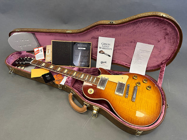 Gibson Les Paul electric guitar with sunburst finish in open brown hardshell case with pink interior, accompanied by Gibson Gold Warranty card, certificates, and tags.