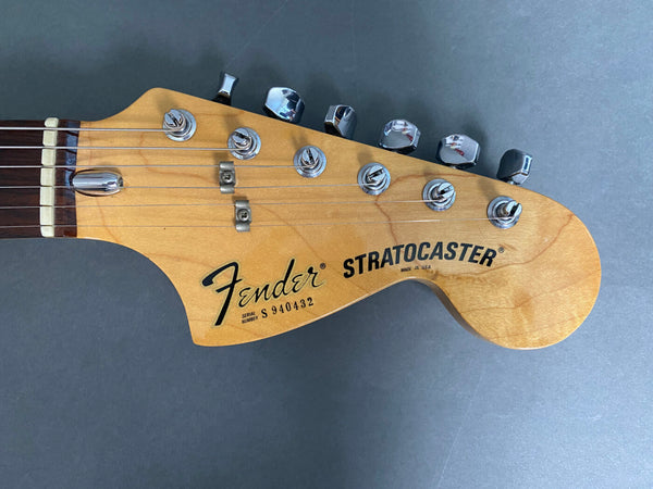 Close-up of Fender Stratocaster guitar headstock with tuning pegs, maple wood finish, and serial number S940432 on gray background