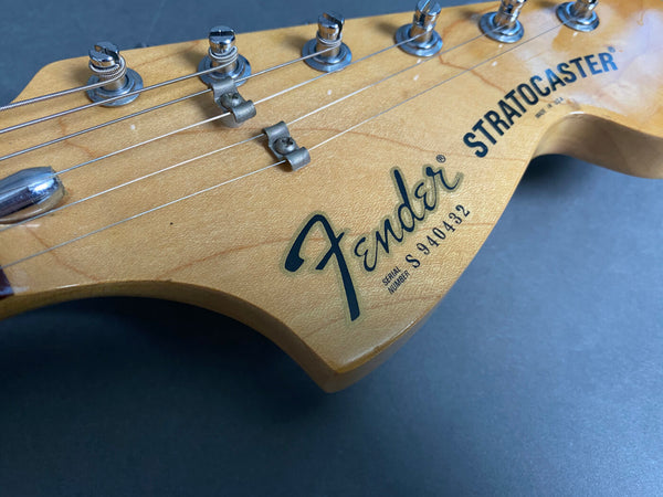 Close-up of Fender Stratocaster electric guitar headstock with serial number S940432 and tuning pegs on natural wood finish