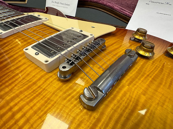 Close-up of a sunburst electric guitar body showing chrome bridge, pickup with cream mounting ring, and amber control knobs on a flamed maple top
