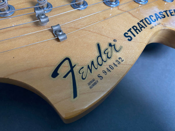 Close-up of Fender Stratocaster guitar headstock showing serial number S940432 and tuning pegs on natural wood finish
