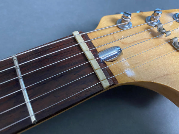 Close-up of guitar headstock showing rosewood fretboard, metal tuning pegs, nut, and strings on a light wood guitar neck