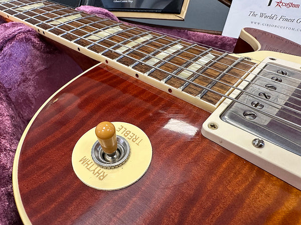 Close-up of Gibson Les Paul electric guitar toggle switch and part of pickguard on reddish sunburst flamed maple top guitar body with rosewood fretboard and metal humbucker pickup.