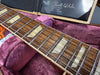 Close-up of Gibson guitar rosewood fretboard with trapezoid inlays and nickel frets inside plush purple guitar case with Gibson Custom Shop certificate