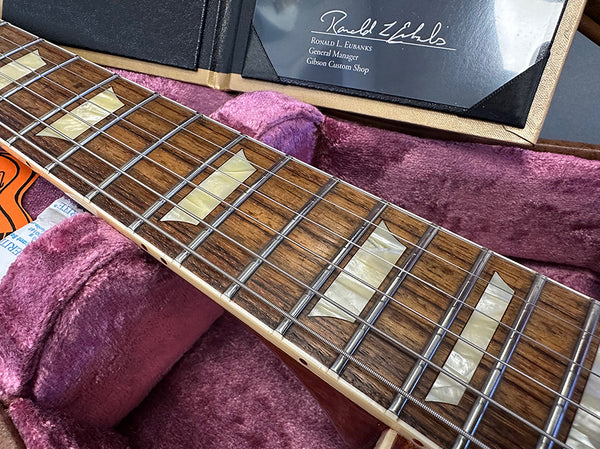 Close-up of Gibson guitar rosewood fretboard with trapezoid inlays and nickel frets inside plush purple guitar case with Gibson Custom Shop certificate