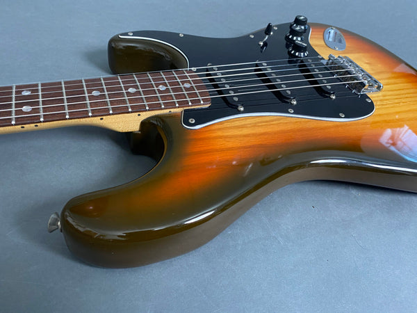 Close-up of sunburst electric guitar body with black pickguard and rosewood fretboard on gray surface