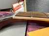 Close-up of guitar neck and nut with six metal strings, showcasing rosewood fretboard and cream binding, with a Gibson tag visible in the background.