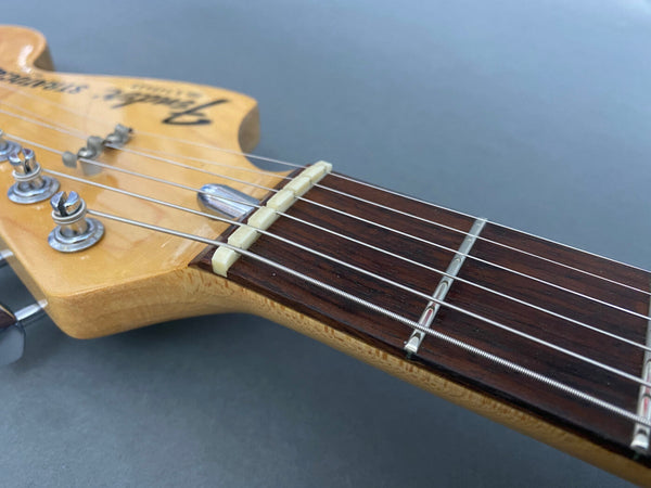 Close-up of Fender Stratocaster electric guitar headstock showing tuning pegs, nut, and rosewood fretboard on gray background
