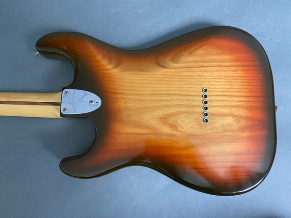 Back view of sunburst electric guitar body with maple neck and six string ferrules on blue background