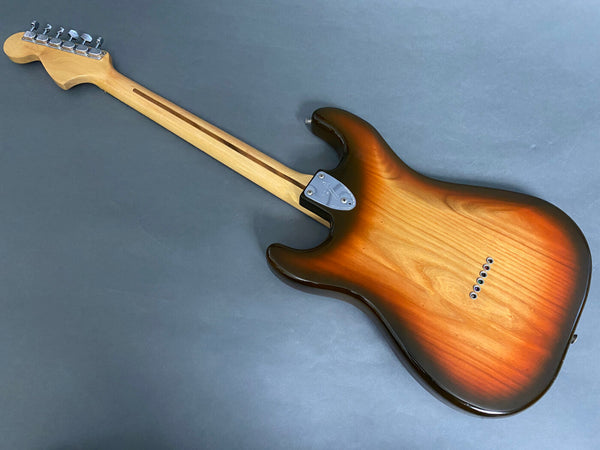 Back view of electric guitar with sunburst finish, maple neck, and six tuning pegs on headstock against gray background