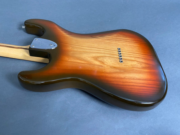 Back view of sunburst finish electric guitar body with string ferrules and maple neck with skunk stripe on blue background