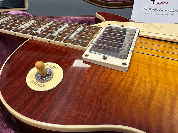 Close-up of cherry sunburst Gibson Les Paul electric guitar body showing rhythm and treble toggle switch, humbucker pickup, and maple neck with rosewood fretboard in guitar case.