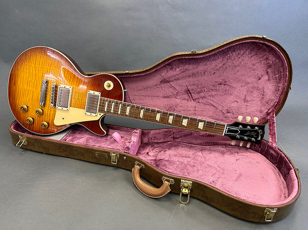 Gibson Les Paul electric guitar with sunburst finish resting in open brown hard case with pink interior lining on gray background