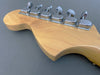 Close-up view of maple guitar headstock with six chrome tuning pegs on gray background, vintage-style tuners with engraved logos