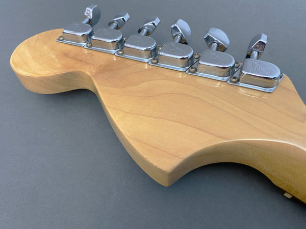 Close-up view of maple guitar headstock with six chrome tuning pegs on gray background, vintage-style tuners with engraved logos