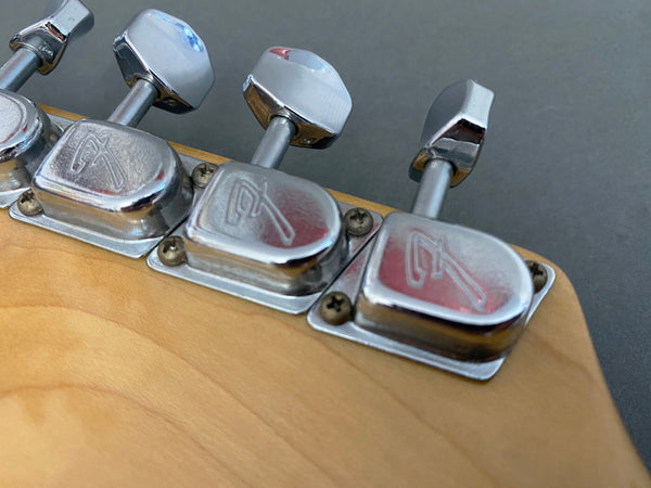 Close-up of vintage Fender guitar tuning pegs with chrome finish on natural wood headstock, showing Fender logo on machine heads