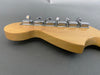 Close-up of natural wood guitar headstock with six chrome tuning pegs against a gray background