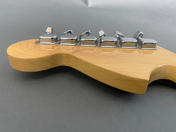 Close-up of natural wood guitar headstock with six chrome tuning pegs against a gray background