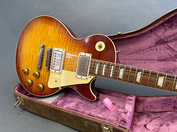 Sunburst electric guitar with dual humbucker pickups resting in an open vintage-style guitar case with plush pink interior, featuring gold control knobs and a wooden fretboard with trapezoid inlays.