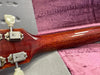 Close-up of guitar neck back showing polished wood grain and vintage tuning pegs on a plush pink and gray guitar case interior